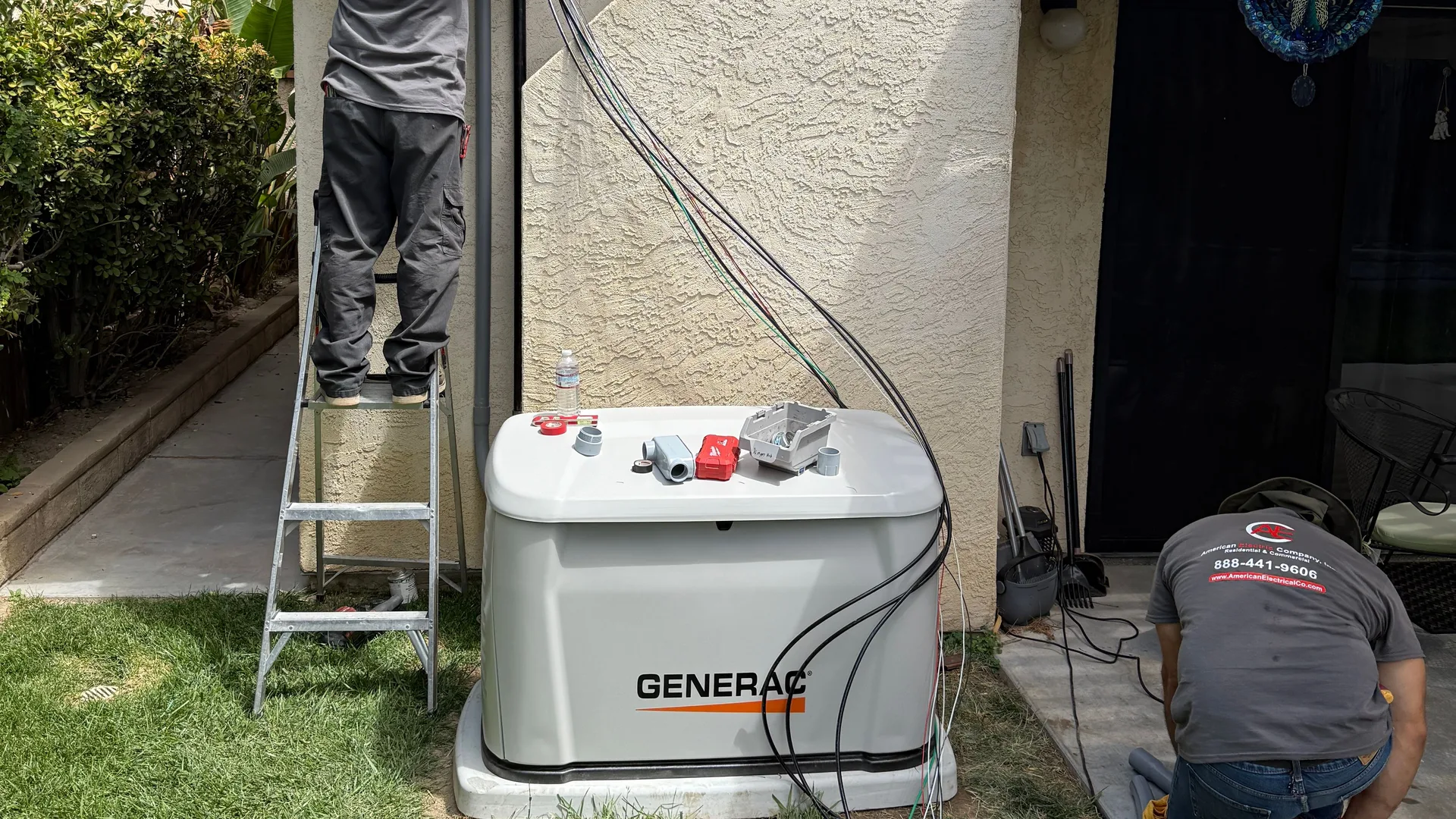 American Electric Co technicians installing a Generac whole-home standby generator beside a house