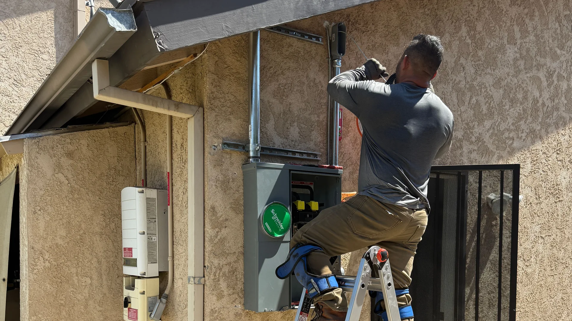 An American Electric Co electrician upgrading an opened exterior main breaker panel from a ladder